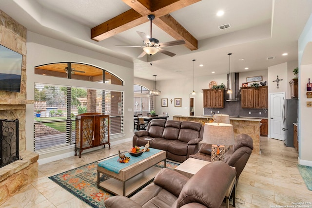 living room with a fireplace, beamed ceiling, and ceiling fan with notable chandelier