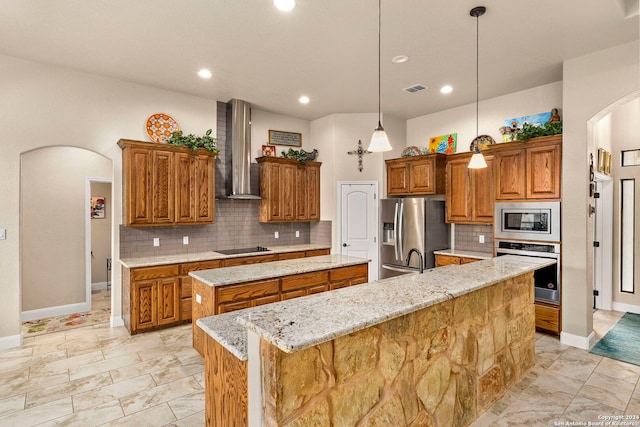 kitchen featuring appliances with stainless steel finishes, tasteful backsplash, an island with sink, wall chimney range hood, and pendant lighting