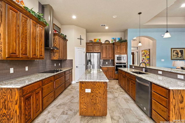 kitchen featuring a kitchen island, wall chimney range hood, appliances with stainless steel finishes, decorative light fixtures, and sink