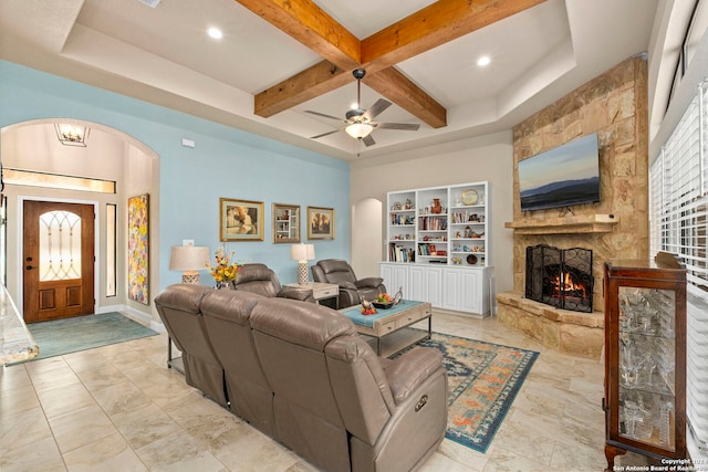 living room featuring a stone fireplace, built in shelves, coffered ceiling, beamed ceiling, and ceiling fan