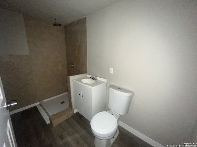 bathroom with toilet, wood-type flooring, a tile shower, and vanity