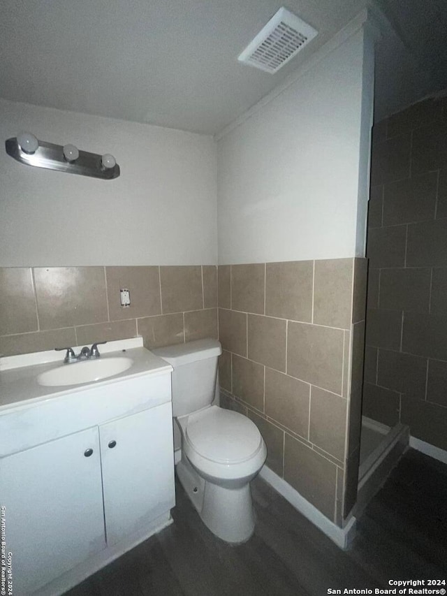 bathroom with walk in shower, vanity, toilet, and tile walls