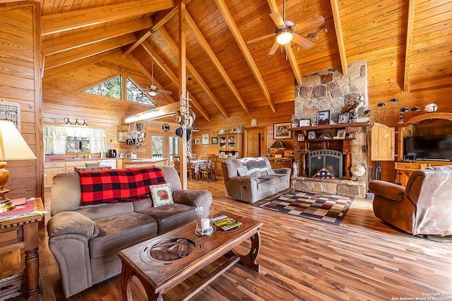 living room with wood ceiling, wood-type flooring, beamed ceiling, a stone fireplace, and wood walls