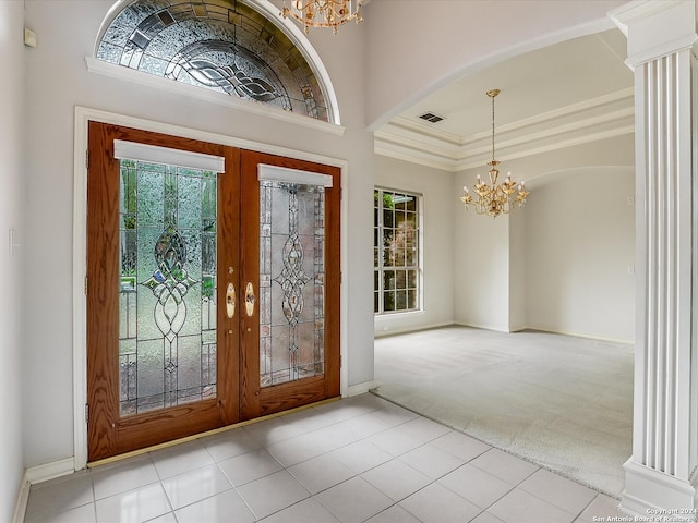 carpeted foyer entrance with decorative columns, a chandelier, french doors, and ornamental molding