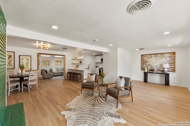 living room with a textured ceiling, light wood-type flooring, and a chandelier