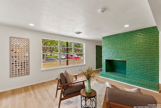 living room featuring a fireplace, light hardwood / wood-style floors, brick wall, and a textured ceiling