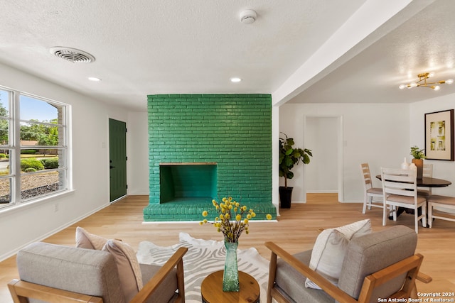 living room featuring a brick fireplace, light hardwood / wood-style floors, a notable chandelier, and a textured ceiling