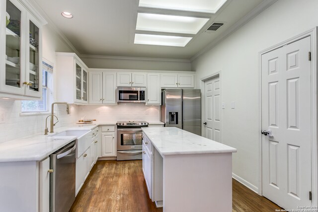 kitchen with white cabinets, appliances with stainless steel finishes, a kitchen island, and dark hardwood / wood-style flooring