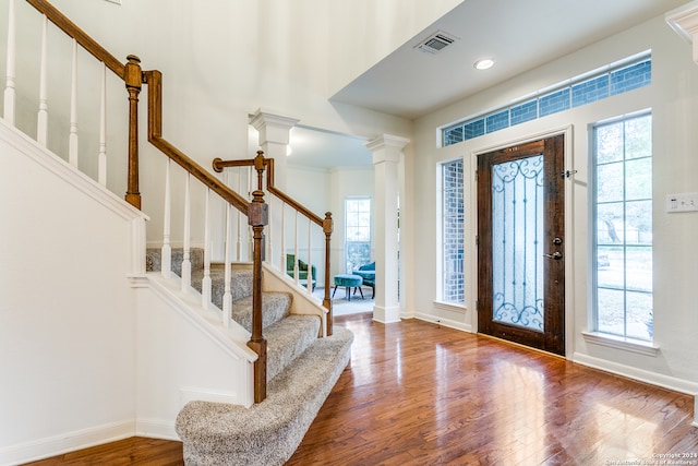 foyer with hardwood / wood-style flooring, crown molding, and decorative columns