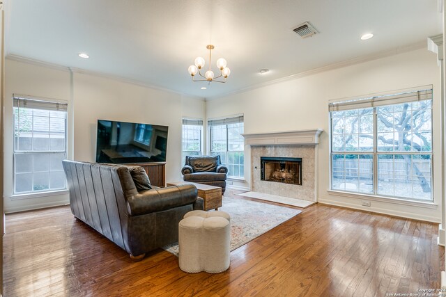 living room featuring hardwood / wood-style floors, a tiled fireplace, plenty of natural light, and crown molding