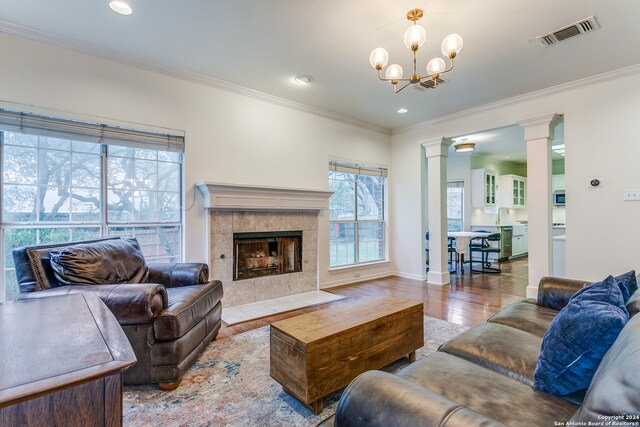 living room with a tiled fireplace, light hardwood / wood-style floors, a healthy amount of sunlight, and crown molding