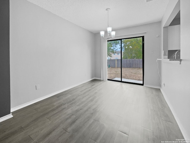 empty room featuring hardwood / wood-style flooring, a textured ceiling, and a notable chandelier