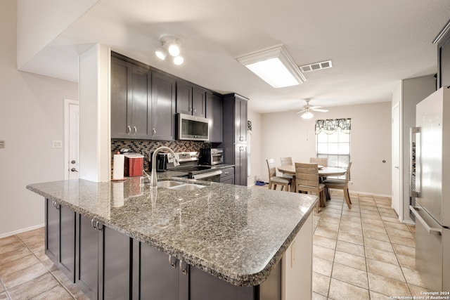 kitchen featuring stainless steel appliances, decorative backsplash, sink, ceiling fan, and dark stone countertops