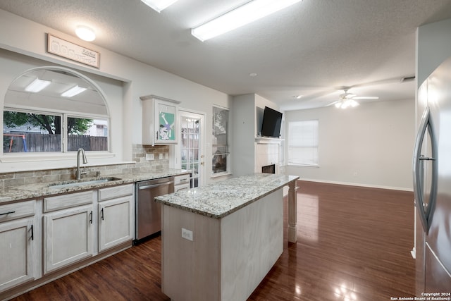 kitchen featuring stainless steel appliances, sink, light stone countertops, a kitchen island, and a tile fireplace