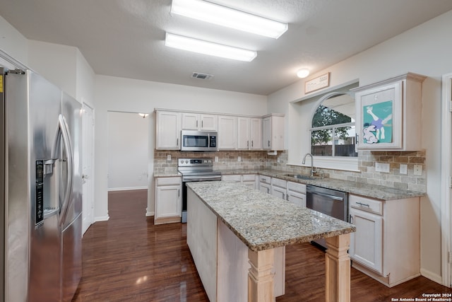 kitchen featuring dark wood-type flooring, light stone counters, sink, a kitchen island, and appliances with stainless steel finishes