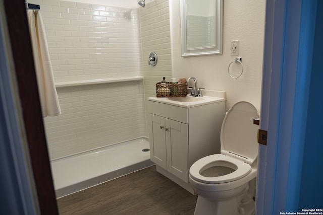 bathroom with hardwood / wood-style flooring, vanity, toilet, and a tile shower