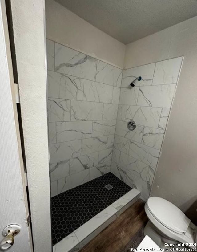 bathroom featuring hardwood / wood-style flooring, toilet, and tiled shower