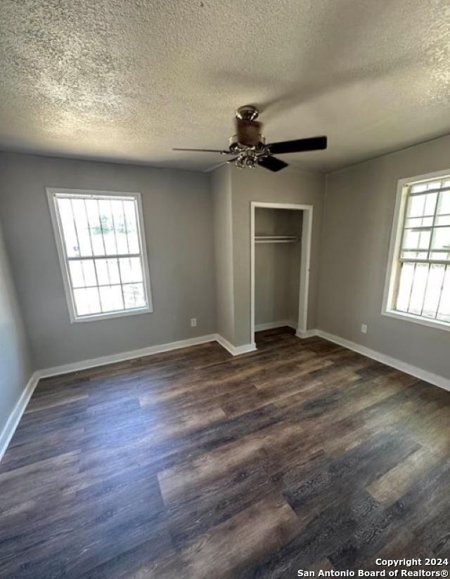 unfurnished bedroom with a textured ceiling, dark hardwood / wood-style flooring, multiple windows, and ceiling fan