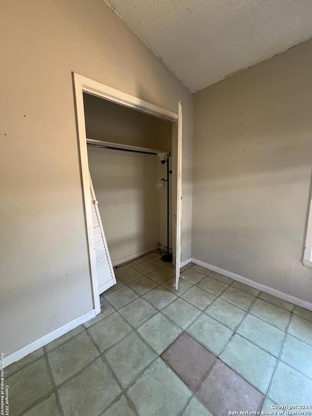 unfurnished bedroom with light tile patterned floors, a textured ceiling, a closet, and lofted ceiling