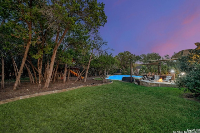 yard at dusk featuring a playground and an outdoor fire pit