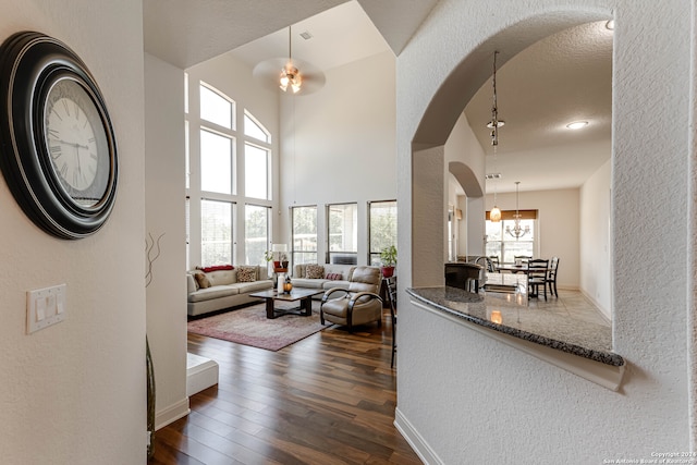 living room featuring a towering ceiling, a textured ceiling, dark hardwood / wood-style floors, and ceiling fan with notable chandelier