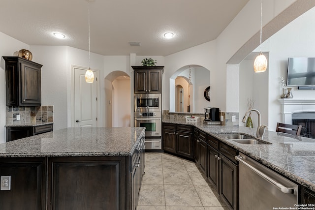 kitchen featuring dark brown cabinetry, sink, appliances with stainless steel finishes, decorative light fixtures, and a center island