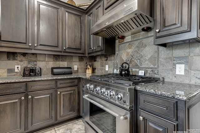 kitchen with tasteful backsplash, extractor fan, high end range, and stone countertops