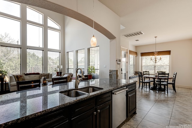 kitchen featuring dark stone counters, decorative light fixtures, stainless steel dishwasher, and sink