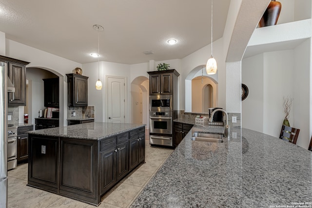 kitchen featuring dark brown cabinetry, sink, kitchen peninsula, appliances with stainless steel finishes, and pendant lighting