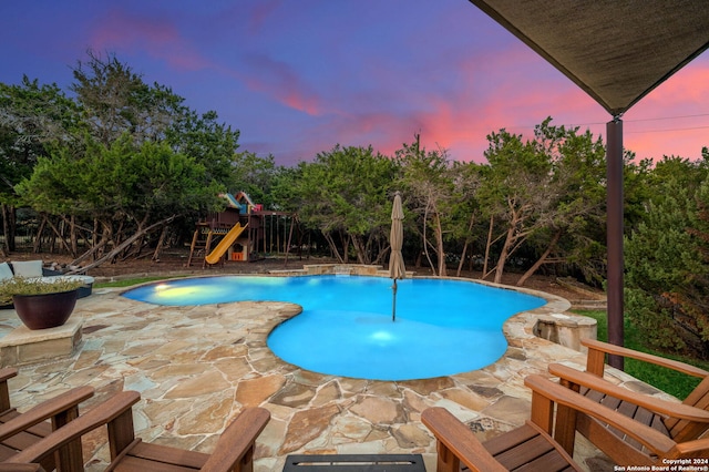 pool at dusk featuring a playground and a patio area