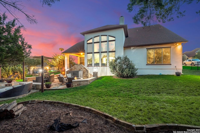 back house at dusk featuring a lawn, a patio, and an outdoor living space with a fire pit