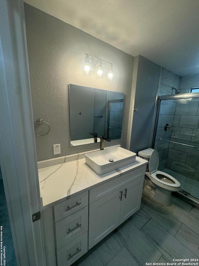 bathroom featuring a shower with door, vanity, toilet, and a textured ceiling