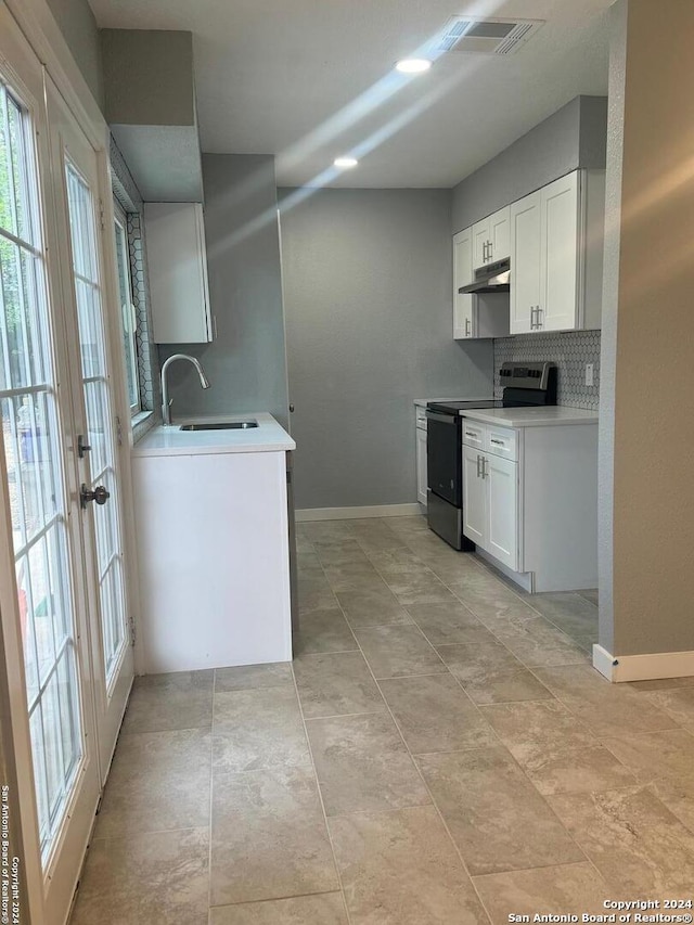 kitchen with stainless steel electric range, white cabinets, sink, and backsplash