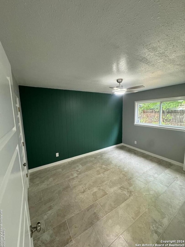 empty room featuring wood walls, ceiling fan, and a textured ceiling