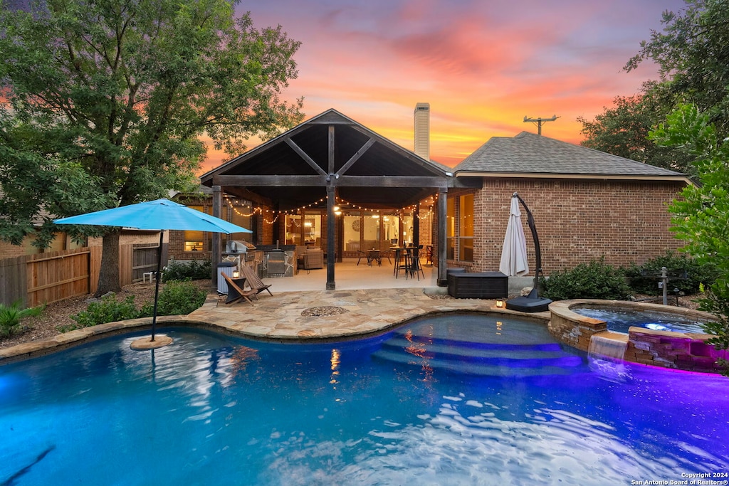 pool at dusk featuring a patio and an in ground hot tub