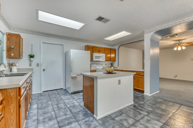 kitchen with white appliances, a textured ceiling, sink, and a center island