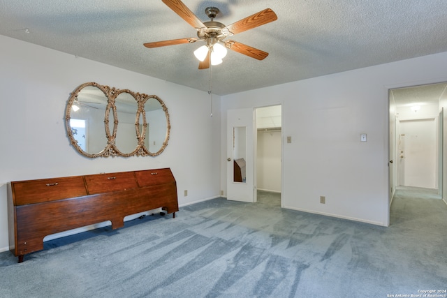 unfurnished bedroom with ceiling fan, a textured ceiling, a spacious closet, light colored carpet, and a closet