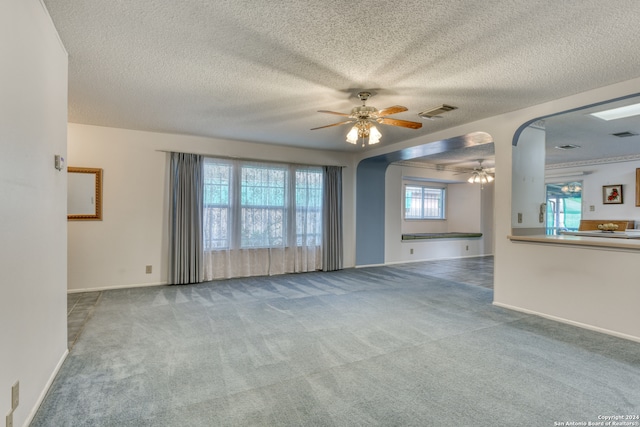 unfurnished living room with a textured ceiling, light carpet, and ceiling fan