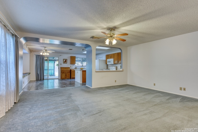 unfurnished living room with a textured ceiling, light carpet, and ceiling fan