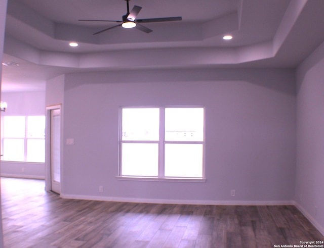 empty room with ceiling fan with notable chandelier, hardwood / wood-style flooring, plenty of natural light, and a tray ceiling