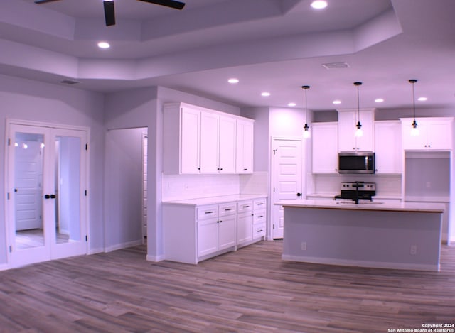 kitchen featuring pendant lighting, white cabinets, a raised ceiling, light hardwood / wood-style floors, and stainless steel appliances