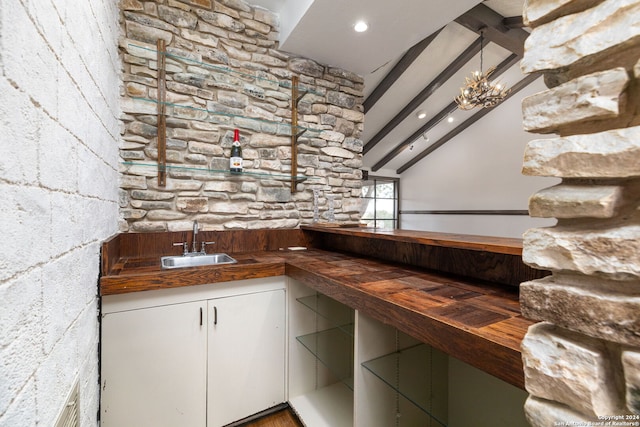 bar with white cabinets, lofted ceiling with beams, sink, and wood counters