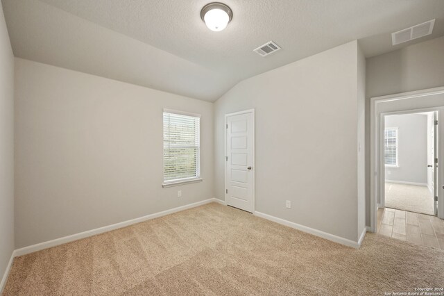 carpeted spare room with a textured ceiling and vaulted ceiling