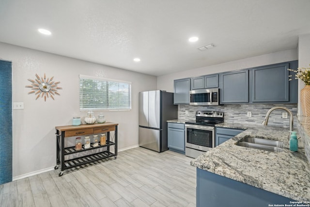 kitchen with tasteful backsplash, stainless steel appliances, light wood-type flooring, light stone countertops, and sink