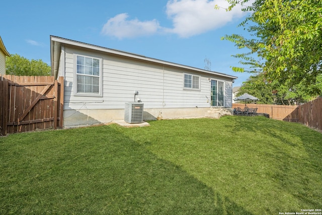 rear view of house with central AC unit and a yard