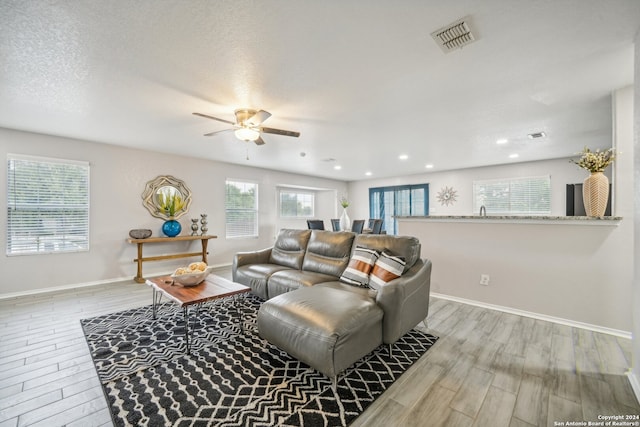 living room with a textured ceiling, light hardwood / wood-style floors, and ceiling fan