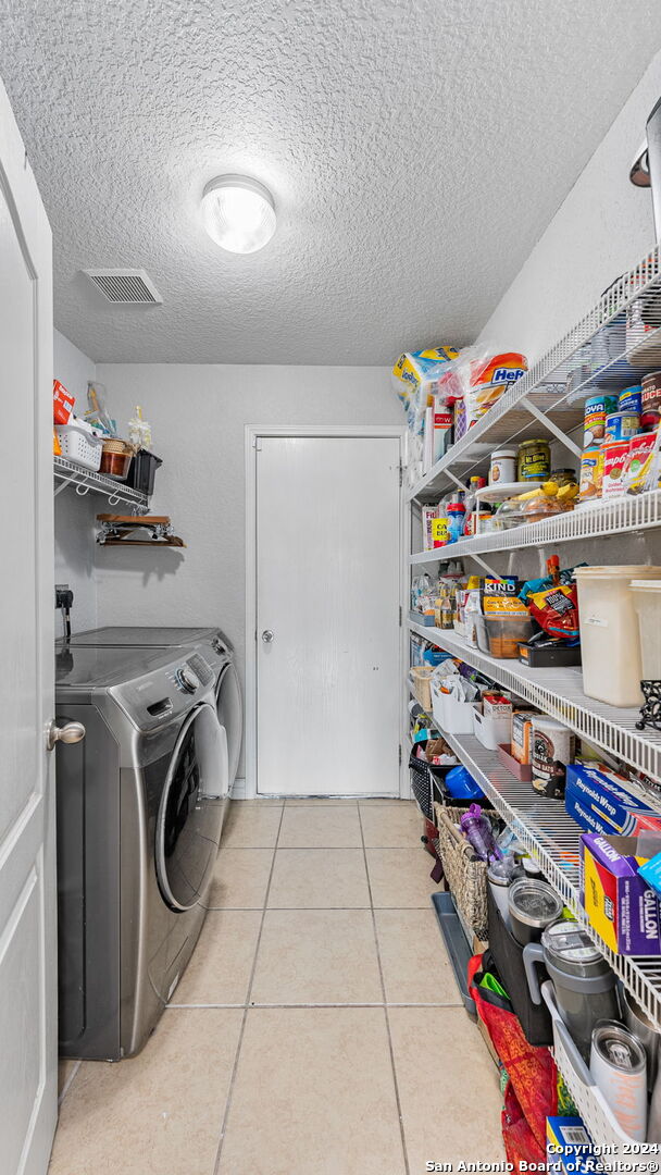 clothes washing area featuring light tile patterned flooring, a textured ceiling, and washer and clothes dryer