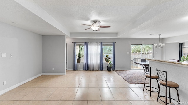 interior space featuring a tray ceiling, a textured ceiling, light tile patterned floors, and ceiling fan with notable chandelier