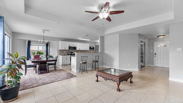 tiled living room featuring ceiling fan with notable chandelier, a textured ceiling, and a tray ceiling