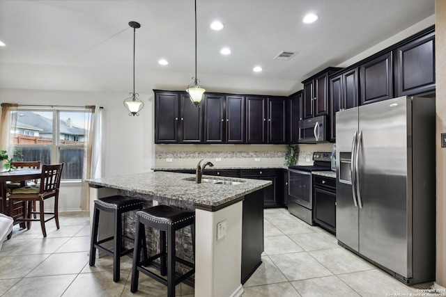 kitchen with stainless steel appliances, light stone countertops, a kitchen bar, a kitchen island with sink, and pendant lighting